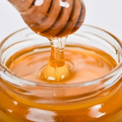 Close-up of honey flowing from a wooden dipper into a glass jar on a white background.